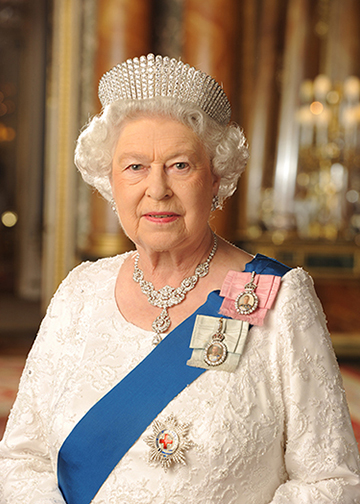 Her Majesty Queen Elizabeth II. An elderly lady with short, curled, white hair. She wears a crown, and a royal sash in blue, a white dress, and a necklace. Her posture and expression are regal and serene.