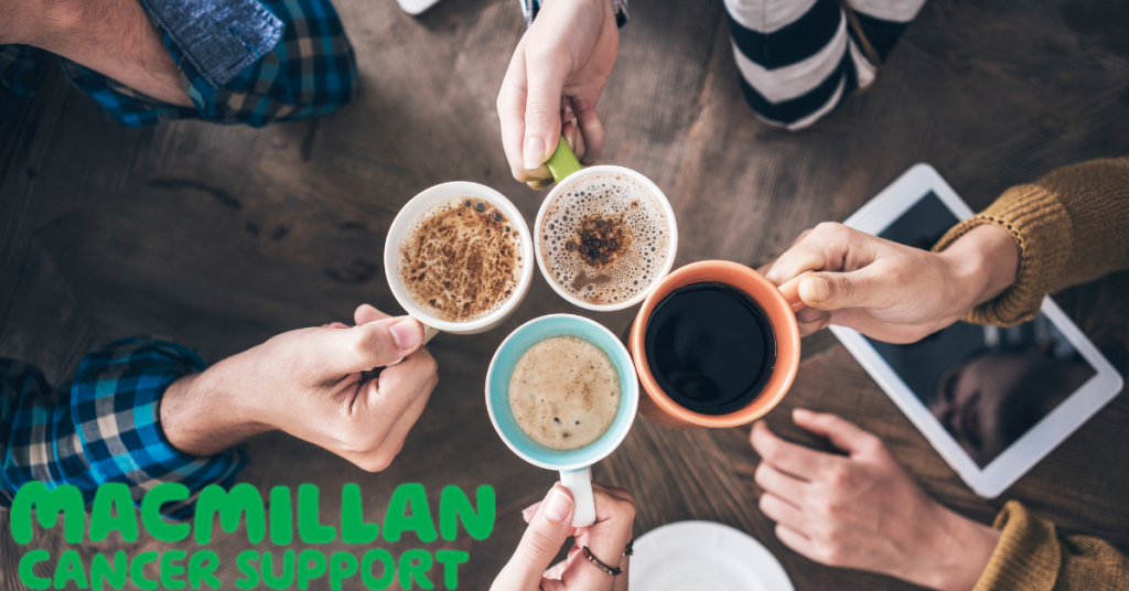 Four cups of coffee in mismatched mugs being held by four hands above a wood floor. In the lower left hand corner is the logo for Macmillan cancer support.